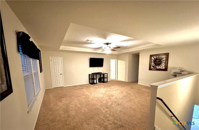 interior space with a tray ceiling, carpet, visible vents, ceiling fan, and an upstairs landing