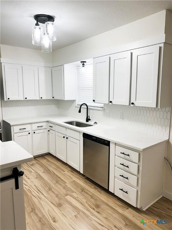 kitchen featuring tasteful backsplash, stainless steel dishwasher, sink, light hardwood / wood-style floors, and white cabinetry