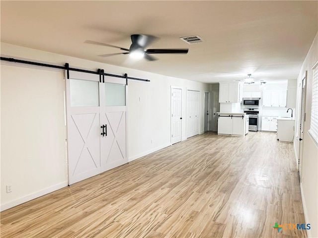 unfurnished living room featuring ceiling fan, a barn door, light hardwood / wood-style floors, and sink