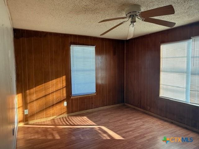 spare room with a wealth of natural light, hardwood / wood-style flooring, ceiling fan, and wood walls