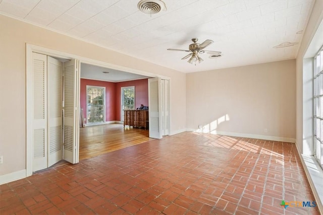 unfurnished room with brick floor, baseboards, visible vents, and a ceiling fan