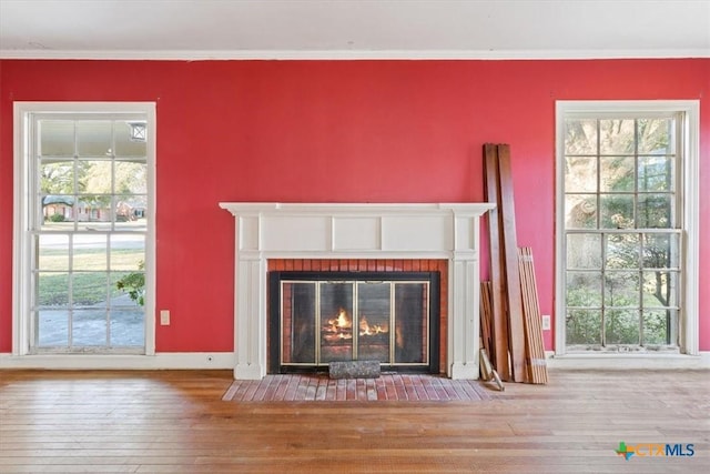 unfurnished living room featuring a brick fireplace, wood-type flooring, a wealth of natural light, and crown molding