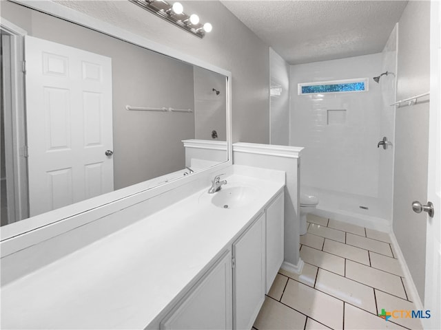 bathroom featuring vanity, tile patterned flooring, toilet, tiled shower, and a textured ceiling