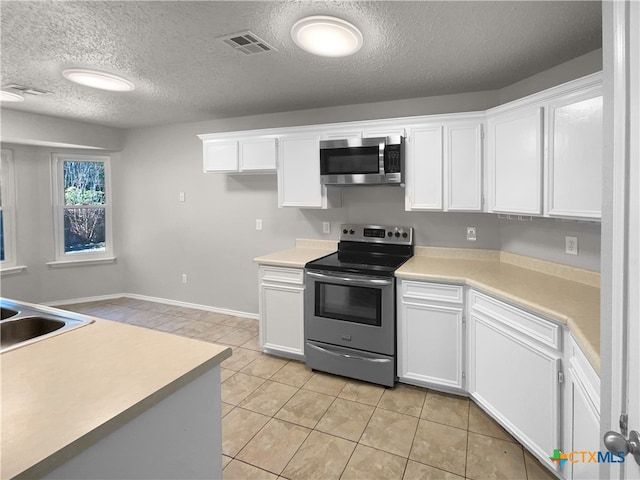 kitchen with sink, a textured ceiling, light tile patterned flooring, white cabinetry, and stainless steel appliances