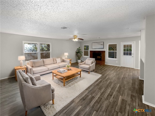 living room with ceiling fan, a fireplace, dark wood-type flooring, and a textured ceiling