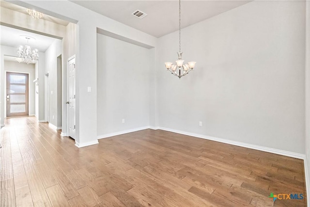 empty room with wood-type flooring and a chandelier