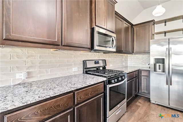 kitchen with appliances with stainless steel finishes, hanging light fixtures, tasteful backsplash, dark brown cabinetry, and vaulted ceiling