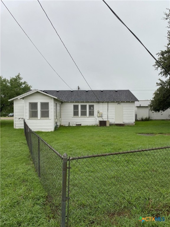 rear view of house with central air condition unit and a lawn