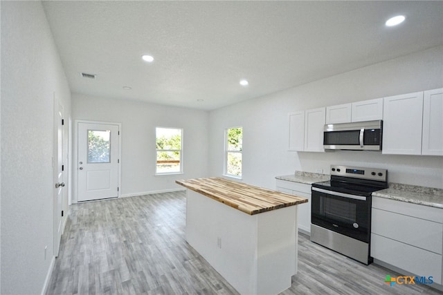 kitchen featuring butcher block countertops, a center island, light wood finished floors, visible vents, and appliances with stainless steel finishes