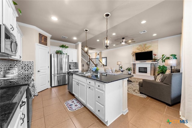 kitchen with decorative backsplash, appliances with stainless steel finishes, ceiling fan, white cabinets, and an island with sink