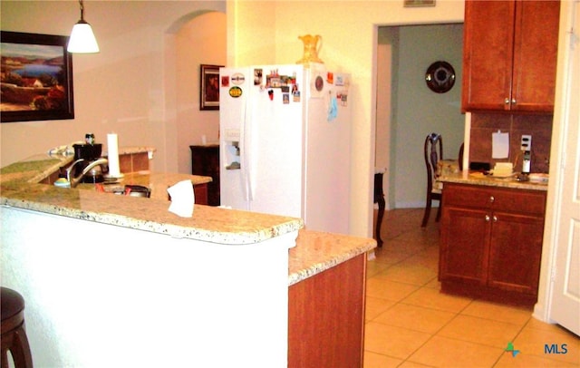 kitchen featuring hanging light fixtures, light tile patterned floors, kitchen peninsula, white refrigerator with ice dispenser, and backsplash