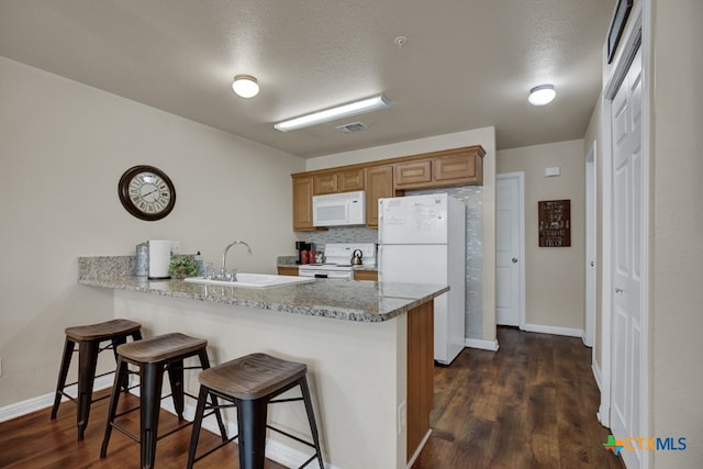 kitchen with sink, light stone counters, a textured ceiling, a kitchen breakfast bar, and white appliances