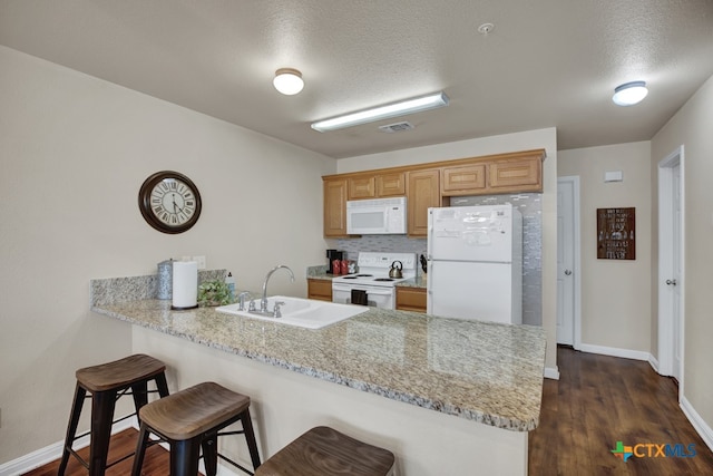 kitchen featuring sink, a textured ceiling, white appliances, and a breakfast bar