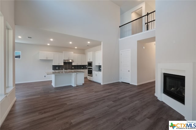 kitchen featuring white cabinetry, appliances with stainless steel finishes, dark hardwood / wood-style flooring, decorative backsplash, and a kitchen island with sink