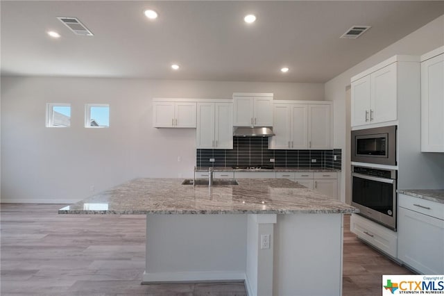 2240 Sur Ave, New Braunfels, TX 78132 - kitchen featuring stainless steel appliances, under cabinet range hood, light stone countertops, white cabinetry, and tasteful backsplash