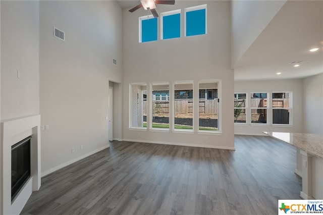 unfurnished living room with ceiling fan, dark hardwood / wood-style floors, and a towering ceiling