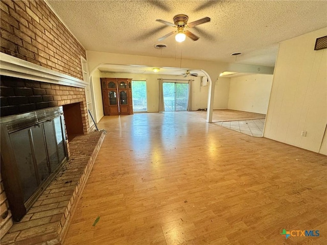 1804 Prather Dr, Killeen, TX 76541 - unfurnished living room featuring a fireplace, arched walkways, a textured ceiling, a ceiling fan, and wood finished floors