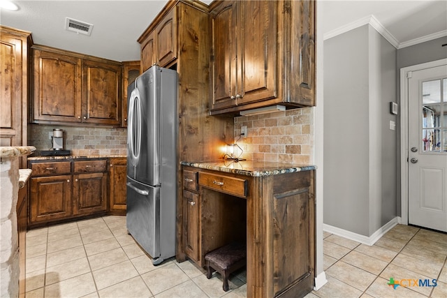 kitchen featuring dark stone counters, stainless steel fridge, crown molding, and decorative backsplash