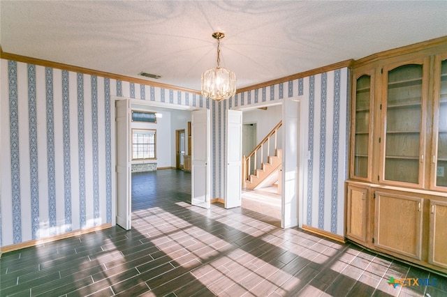 unfurnished dining area featuring dark wood-type flooring, a textured ceiling, crown molding, and a notable chandelier