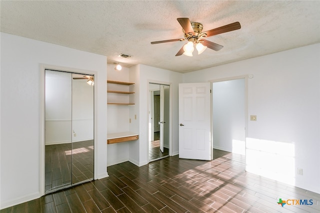 unfurnished bedroom with ceiling fan, a textured ceiling, multiple closets, and dark hardwood / wood-style flooring