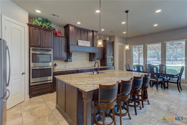 2326 Haven Bluff Ct, New Braunfels, TX 78132 - kitchen featuring appliances with stainless steel finishes, a sink, tasteful backsplash, light stone countertops, and a kitchen island with sink