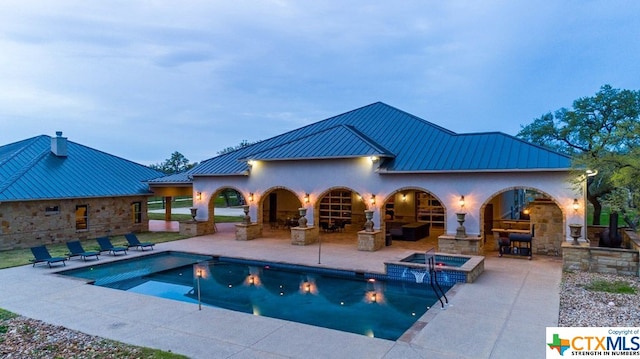 pool at dusk featuring an in ground hot tub and a patio area