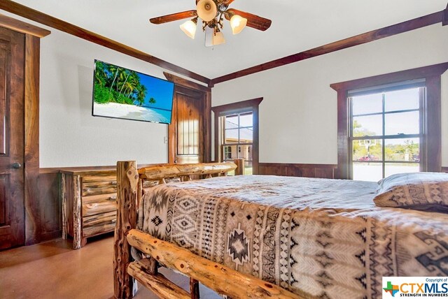 bedroom featuring multiple windows, wooden walls, ceiling fan, and crown molding