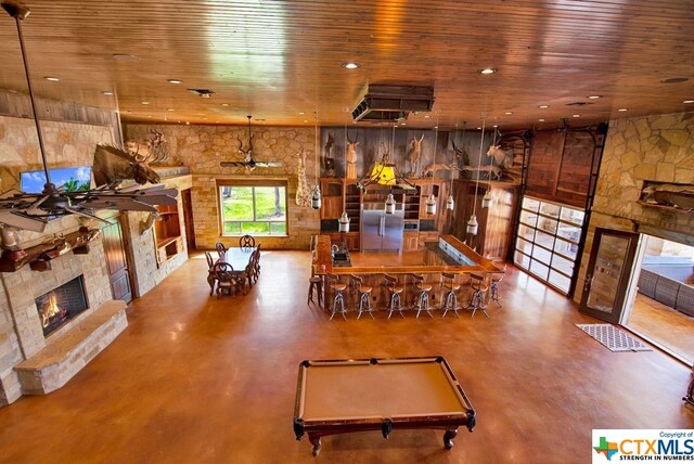 dining space with ceiling fan, a stone fireplace, wood ceiling, and concrete floors