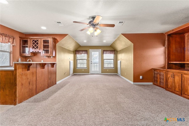 interior space featuring light countertops, a ceiling fan, brown cabinetry, light carpet, and a kitchen bar