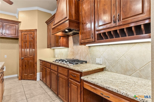 kitchen featuring light tile patterned floors, tasteful backsplash, light stone counters, crown molding, and stainless steel gas stovetop