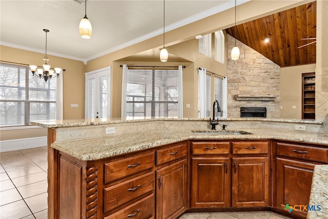 kitchen featuring hanging light fixtures, light stone countertops, brown cabinets, and a sink