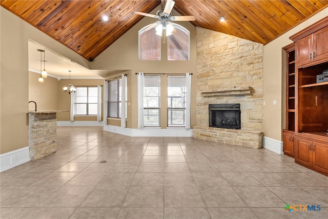 unfurnished living room featuring wood ceiling, light tile patterned floors, a stone fireplace, and ceiling fan with notable chandelier