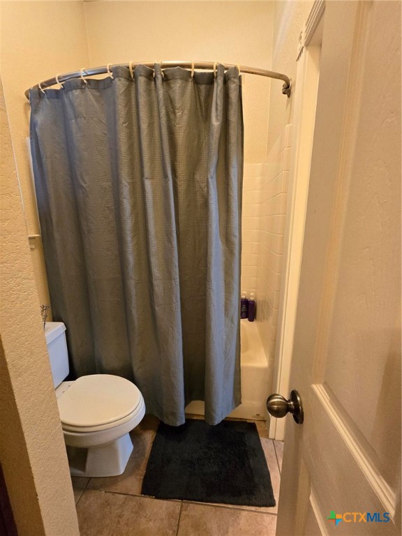 bathroom featuring tile patterned flooring, shower / bath combination with curtain, and toilet