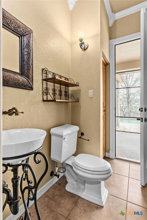 half bathroom with toilet, tile patterned flooring, baseboards, and crown molding