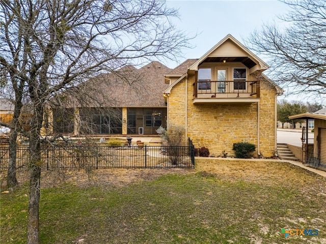 back of house with a shingled roof, a lawn, fence, a balcony, and stone siding