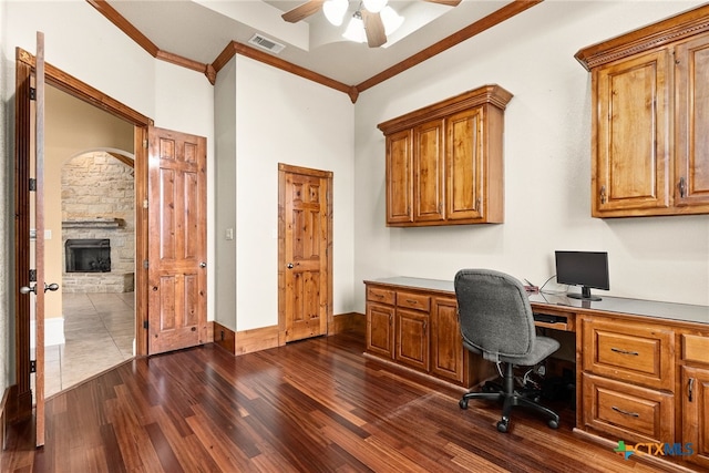 home office featuring dark wood-type flooring, a fireplace, visible vents, a ceiling fan, and ornamental molding