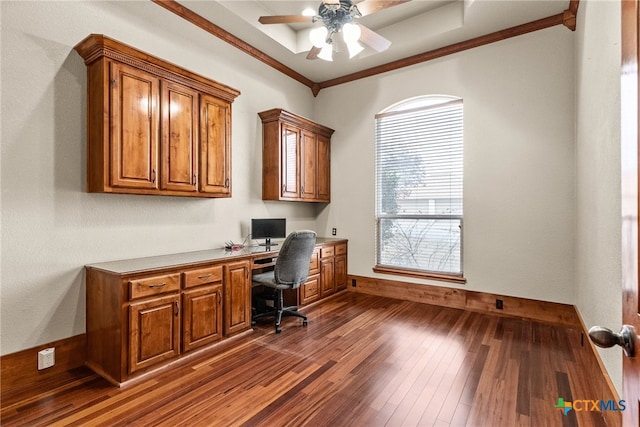 office space with built in desk, dark wood-type flooring, ornamental molding, a ceiling fan, and baseboards