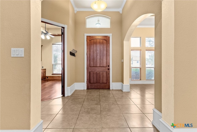 entryway featuring baseboards, ornamental molding, arched walkways, and light tile patterned flooring