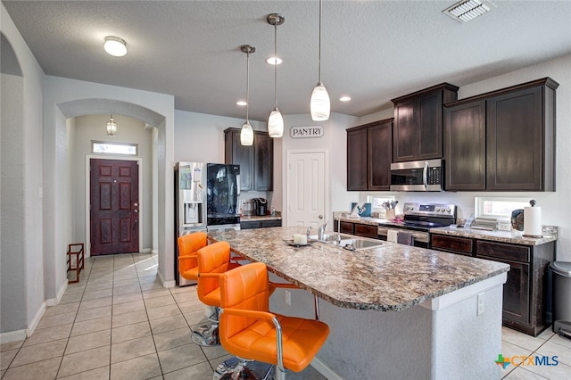 kitchen featuring stainless steel appliances, dark brown cabinetry, a textured ceiling, sink, and an island with sink