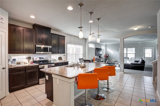 kitchen featuring appliances with stainless steel finishes, decorative light fixtures, a kitchen bar, sink, and a kitchen island with sink