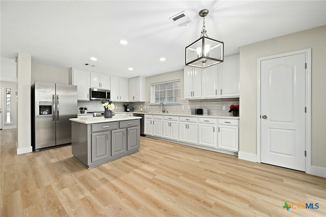 kitchen featuring stainless steel appliances, a notable chandelier, a center island, white cabinetry, and hanging light fixtures