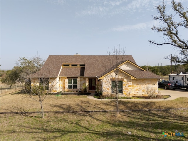 view of front facade with a front lawn, stone siding, and roof with shingles