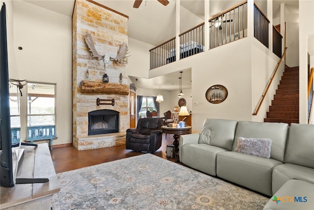 living room featuring a stone fireplace, stairs, a high ceiling, and ceiling fan