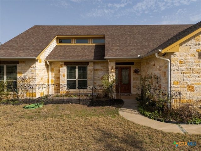 view of front of house with a front lawn, stone siding, and a shingled roof