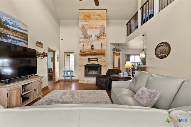 living room with a stone fireplace, wood finished floors, baseboards, and a towering ceiling