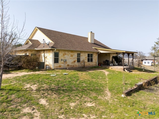 rear view of property featuring roof with shingles, a lawn, cooling unit, a chimney, and stone siding