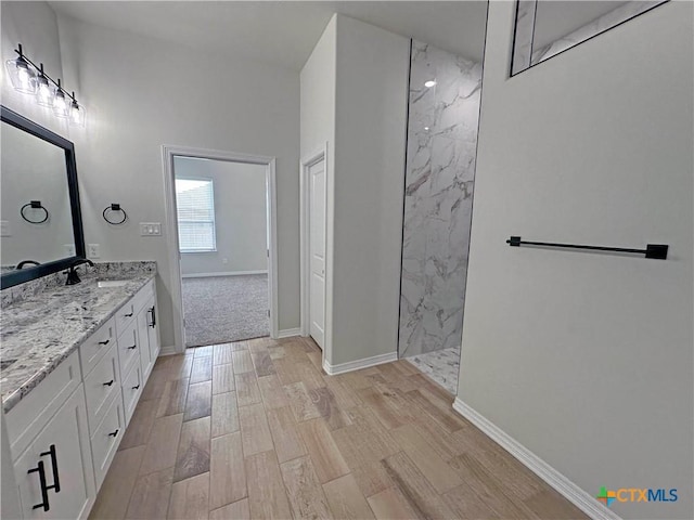 bathroom with a marble finish shower, wood finished floors, vanity, and baseboards