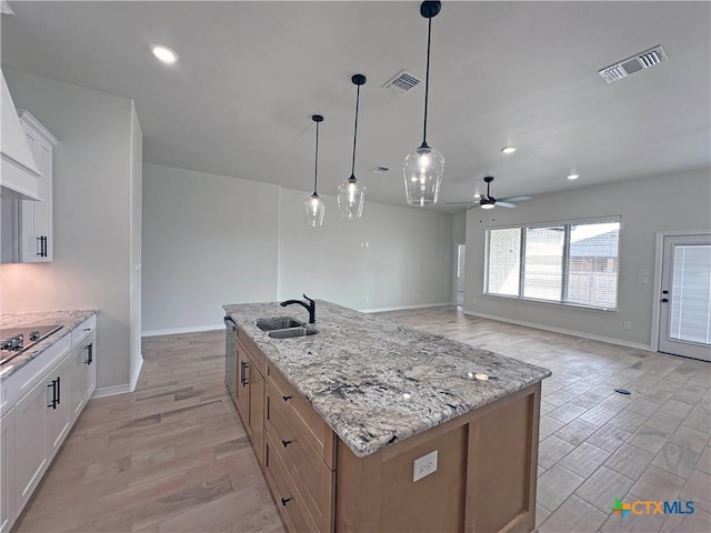 kitchen with black electric stovetop, a center island with sink, visible vents, and a sink