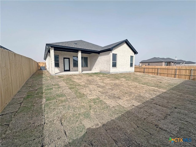 rear view of property featuring a fenced backyard, a lawn, and brick siding