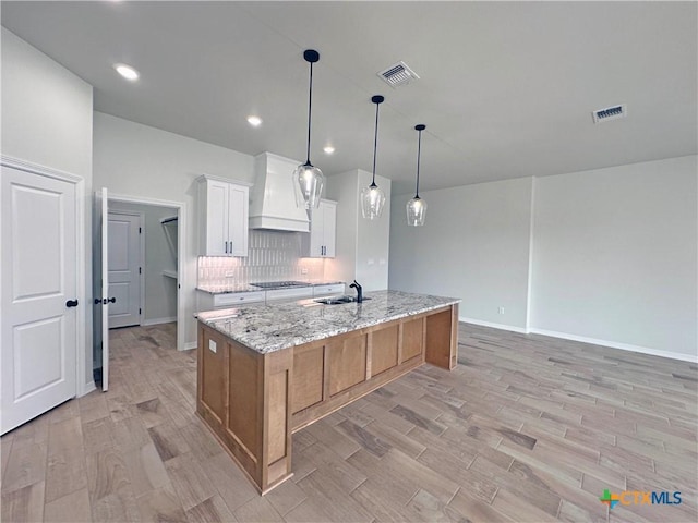 kitchen featuring premium range hood, visible vents, black electric cooktop, and a sink